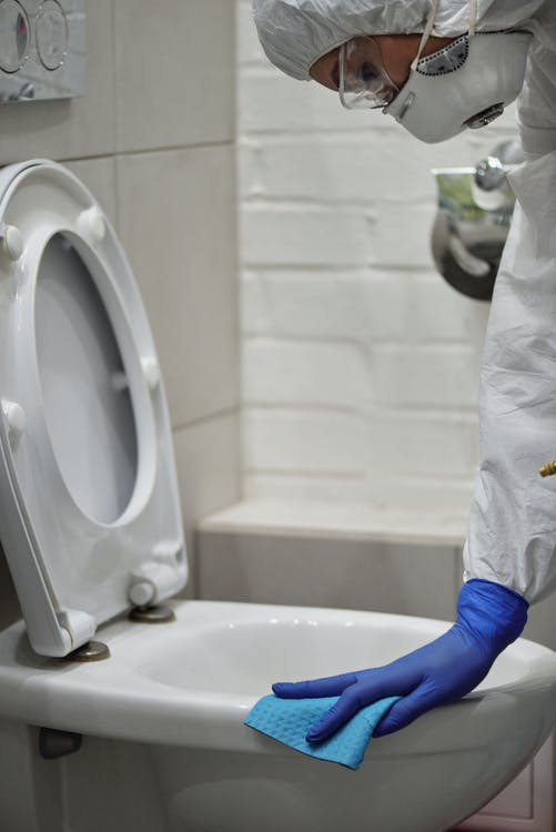 A person wearing PPE and cleaning a bathroom